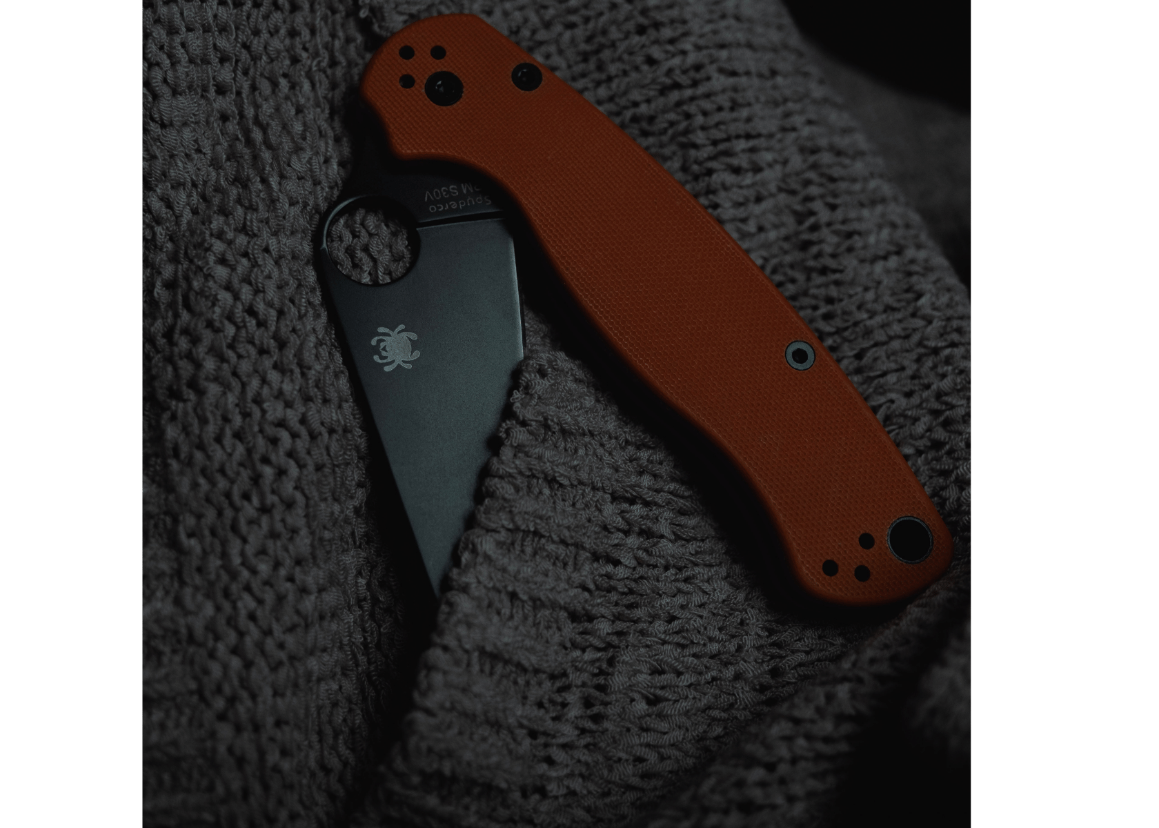 A Spyderco EDC knife with black blade and red handles on a grey sweater.