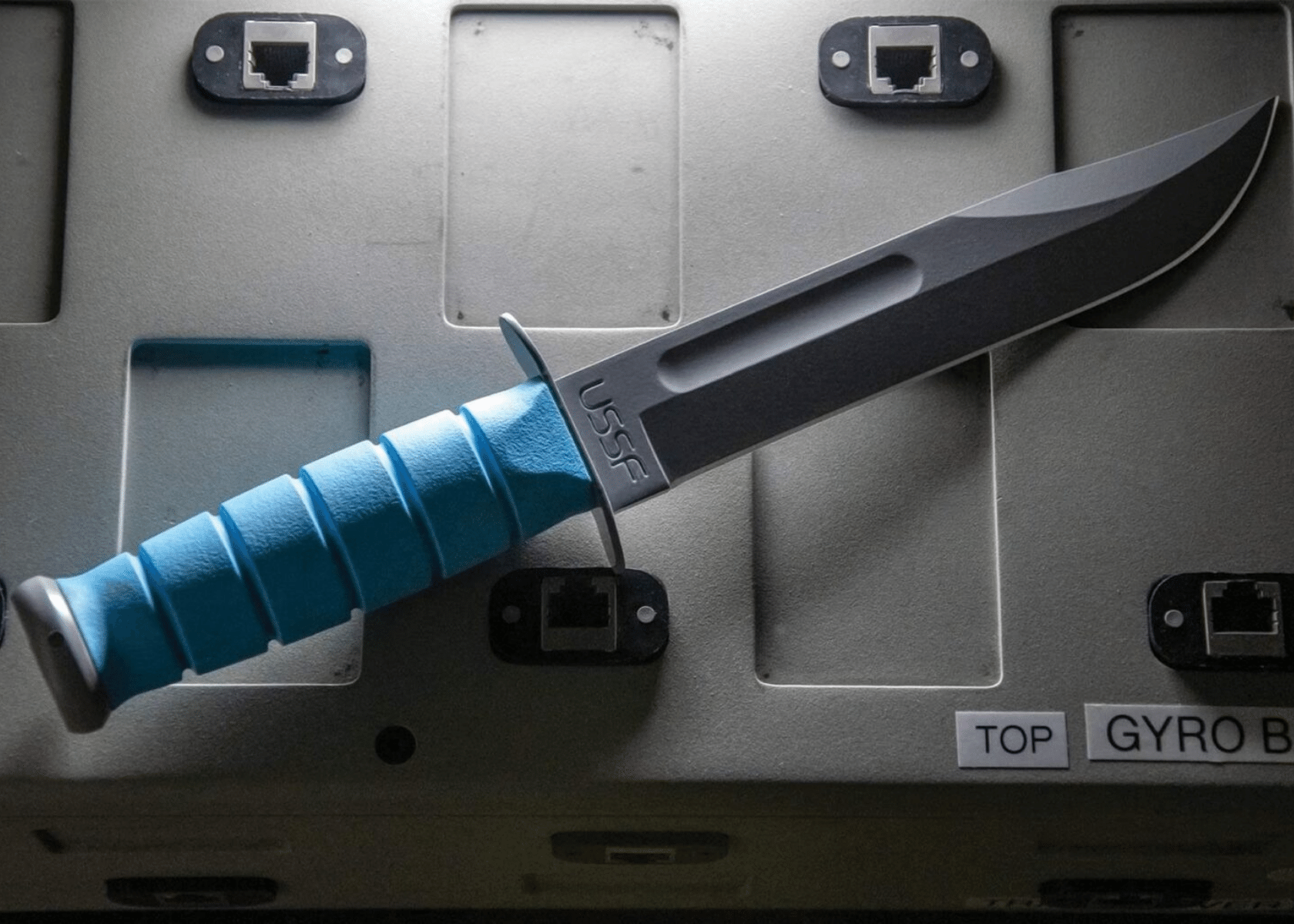 A version of the KA-BAR fighting knife with a blue handle on a cargo crate.