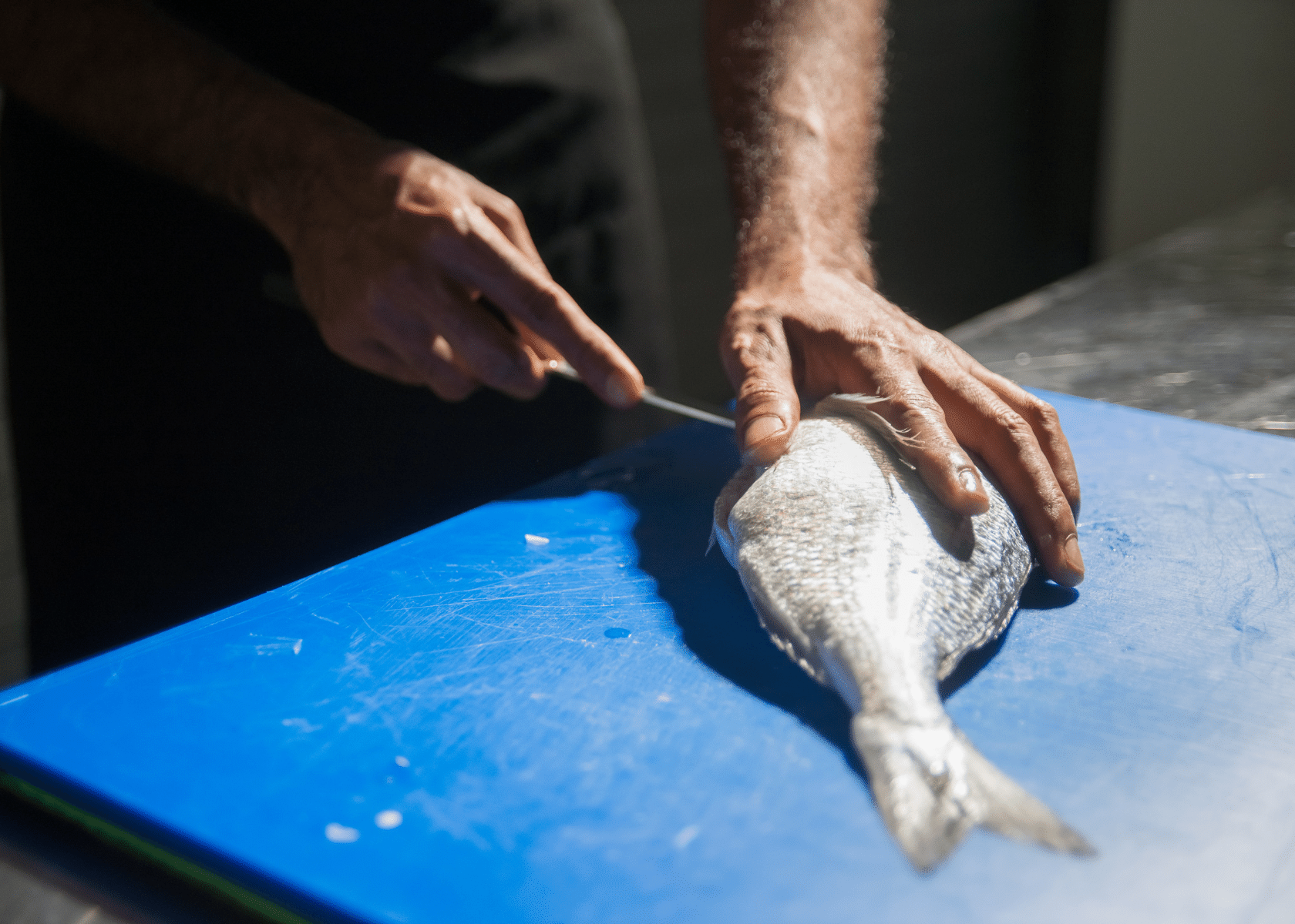 A man filleting a fish on a blue table with a fillet knife.