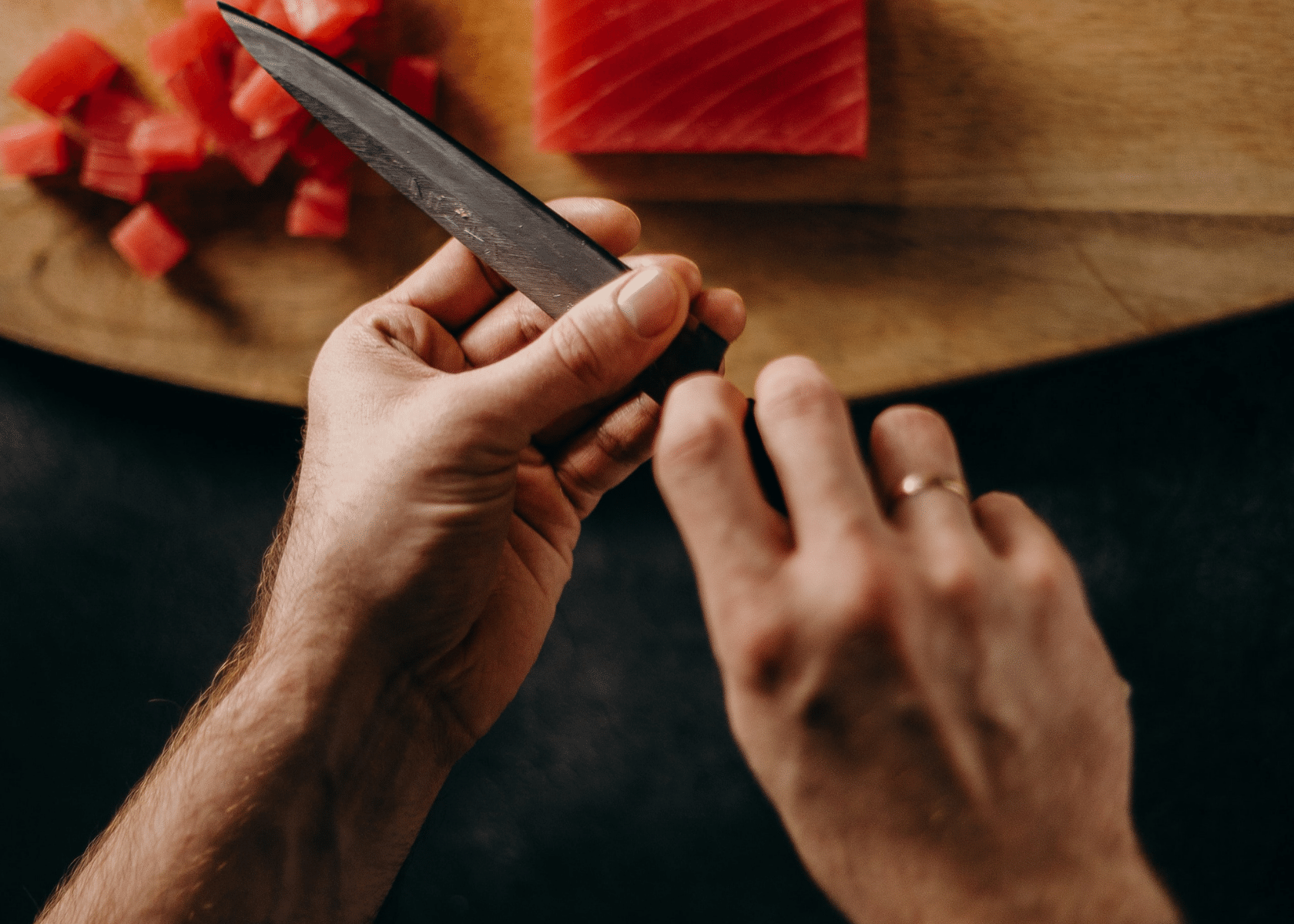 A man wiping a chefs knife with his fingers looking over some freshly cut fish.