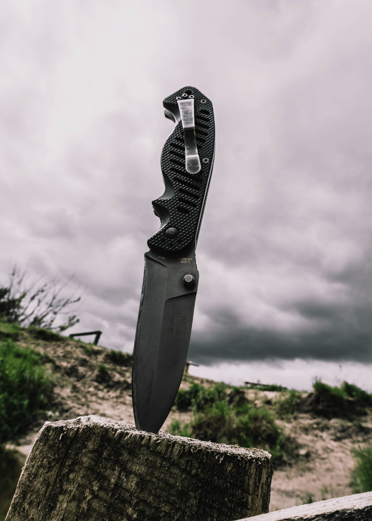 A close up of the knife stabbed into a fence post on a hill looking up at the cloudy sky