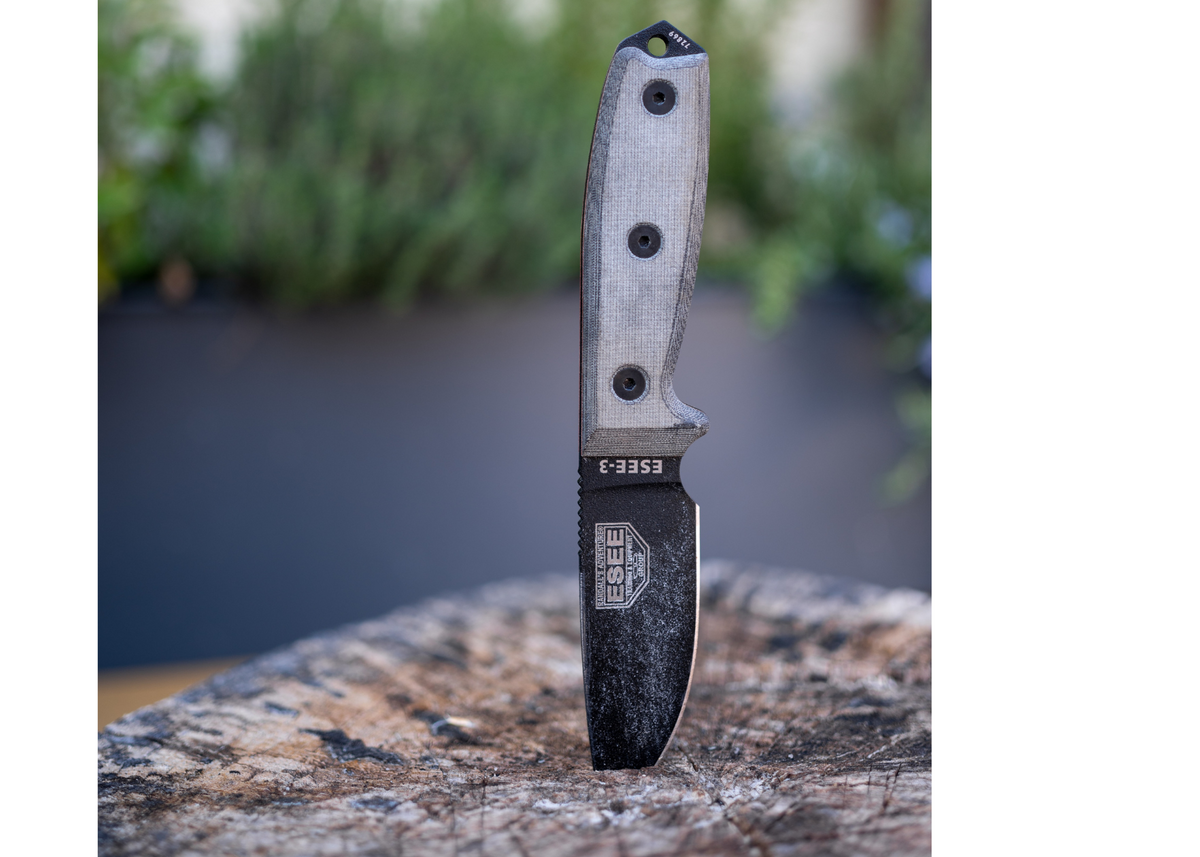 An ESEE Bushcraft knife stabbed down into a wood block with the background out of focus