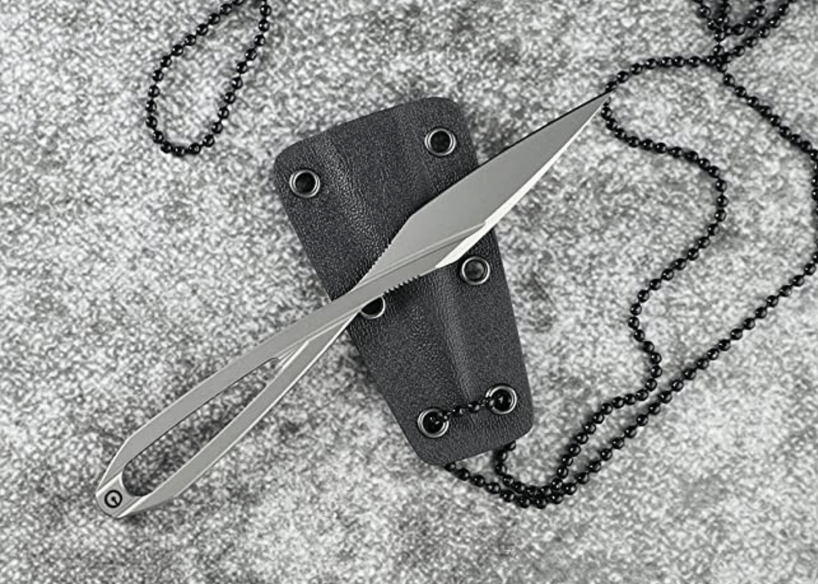 A skeletonized neck knife with Kydex holster and chain on grey carpet