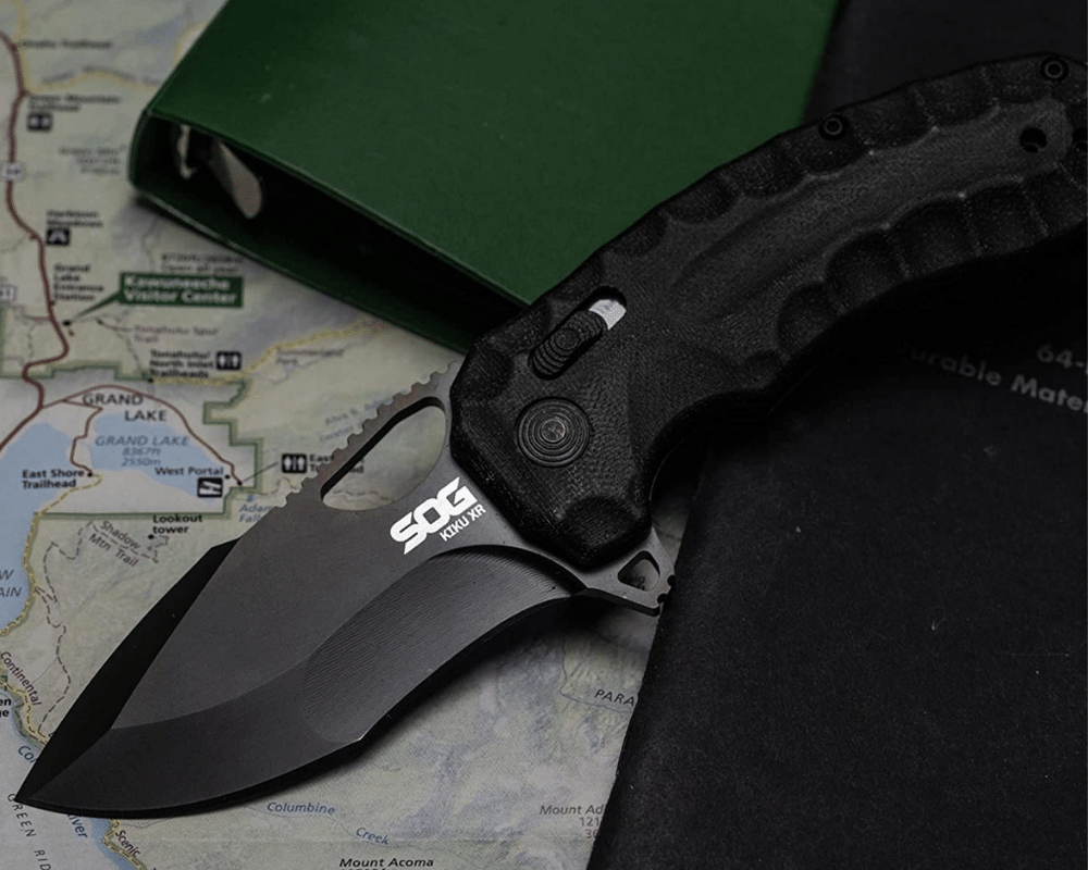 A SOG Tanto knife laying on a map and a folder