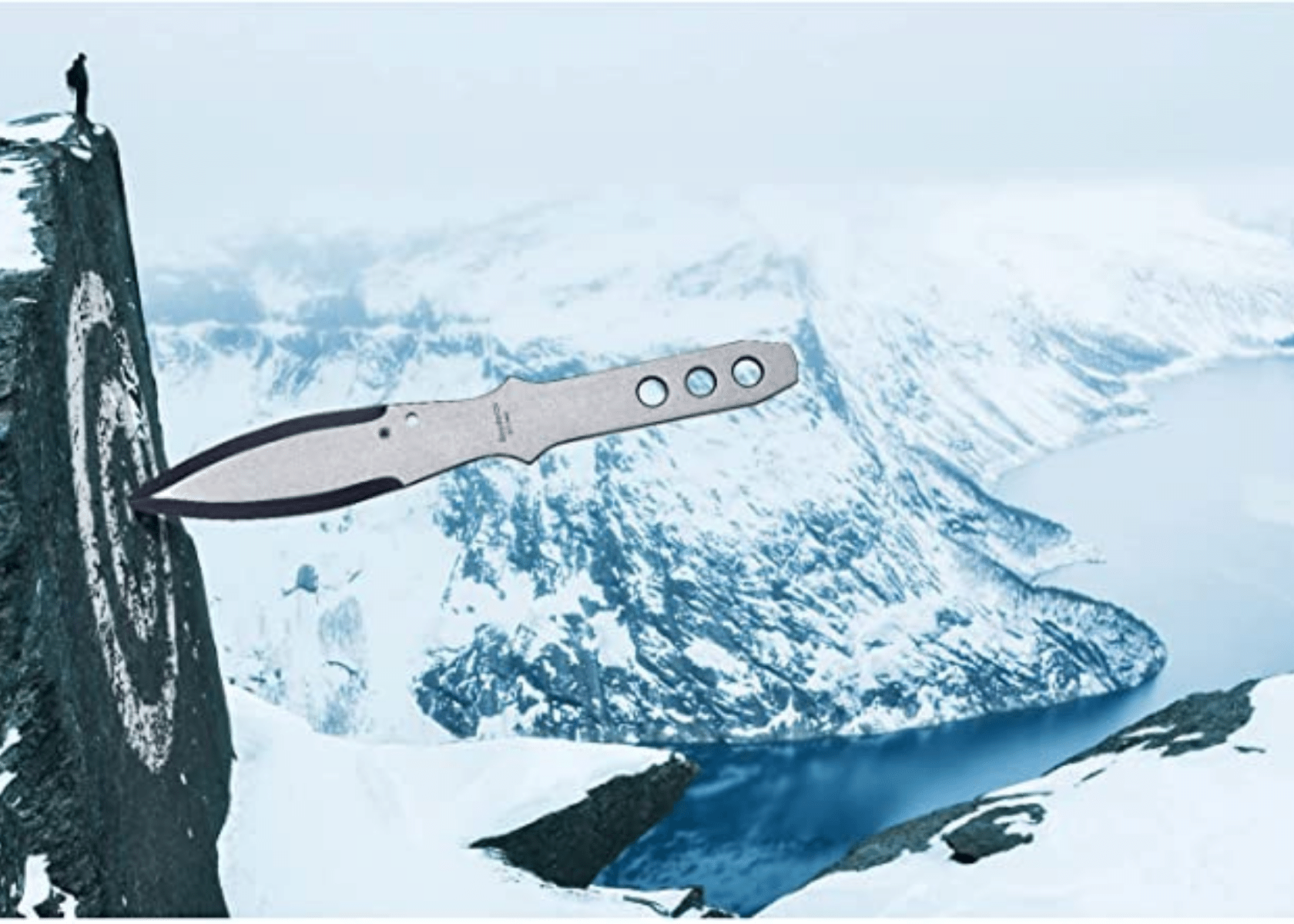 A throwing knife with a target that has been created on a mountain side with snowy mountains in the background