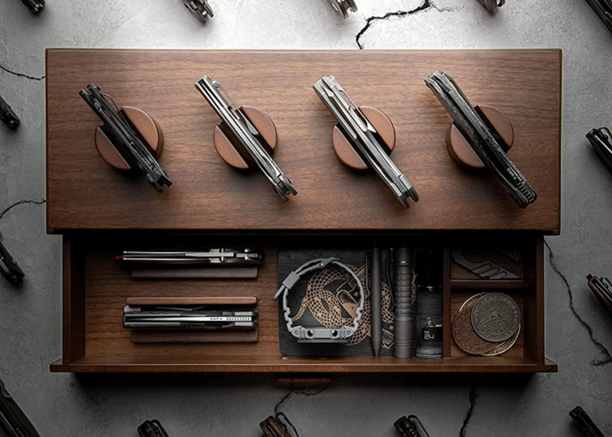 A wooden display case with a drawer for knives and other EDC items and 4 individual knife holders on top.