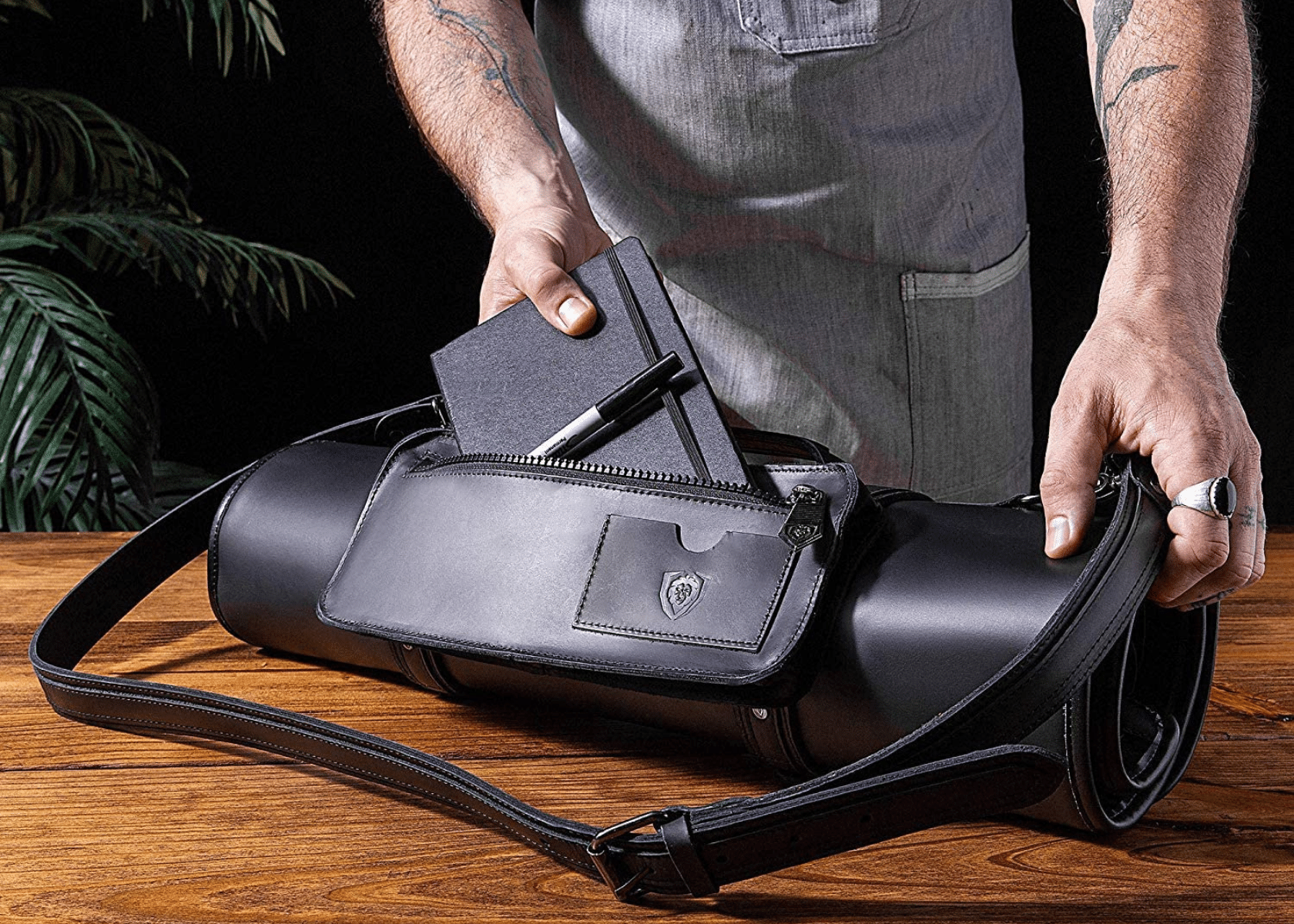 A man loading his leather knife roll with a notebook on a wood table