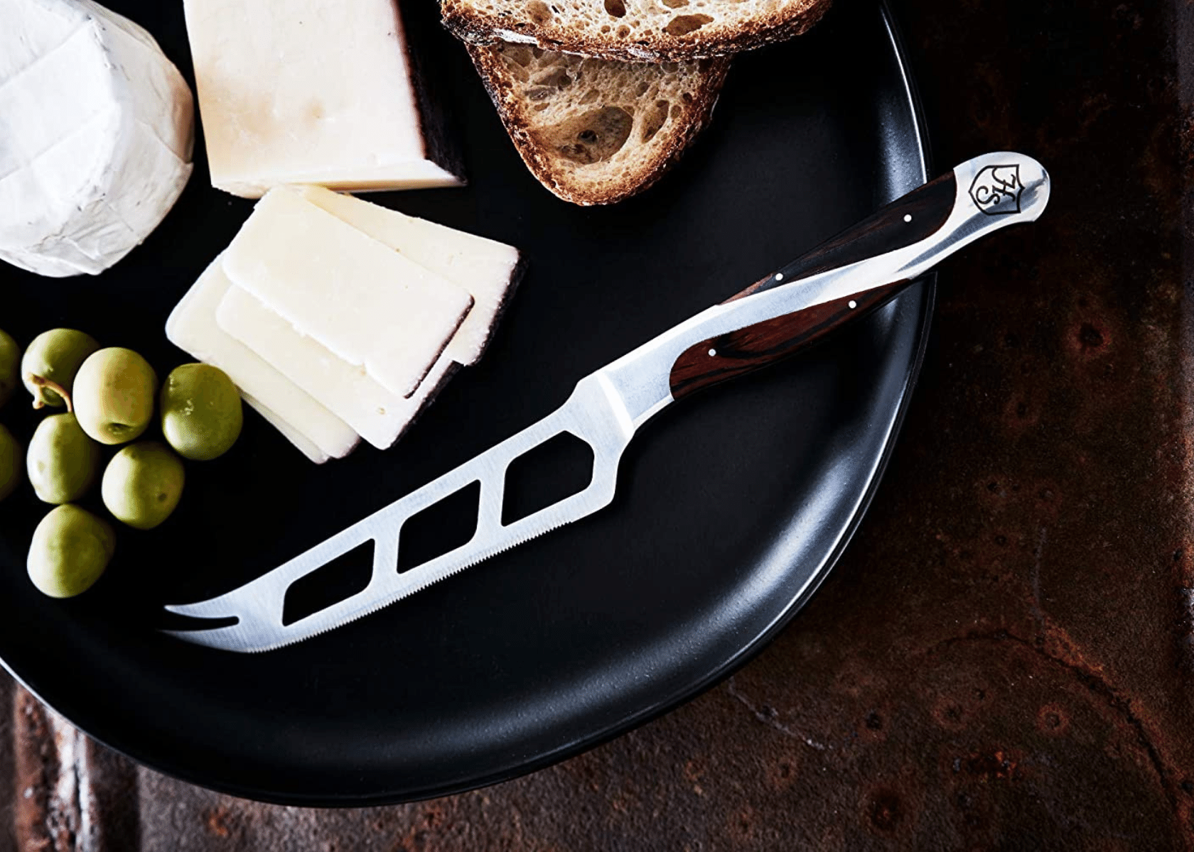 A cheese knife and cheese with grapes and bread on a serving platter