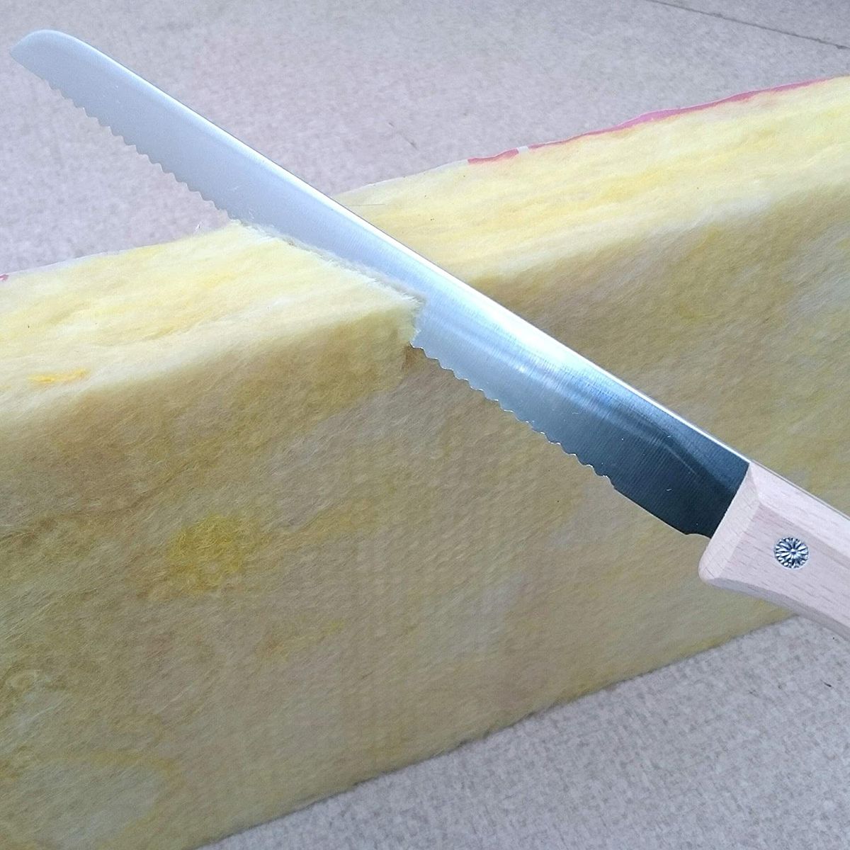 A serrated blade horizontally cutting a piece of insulation.