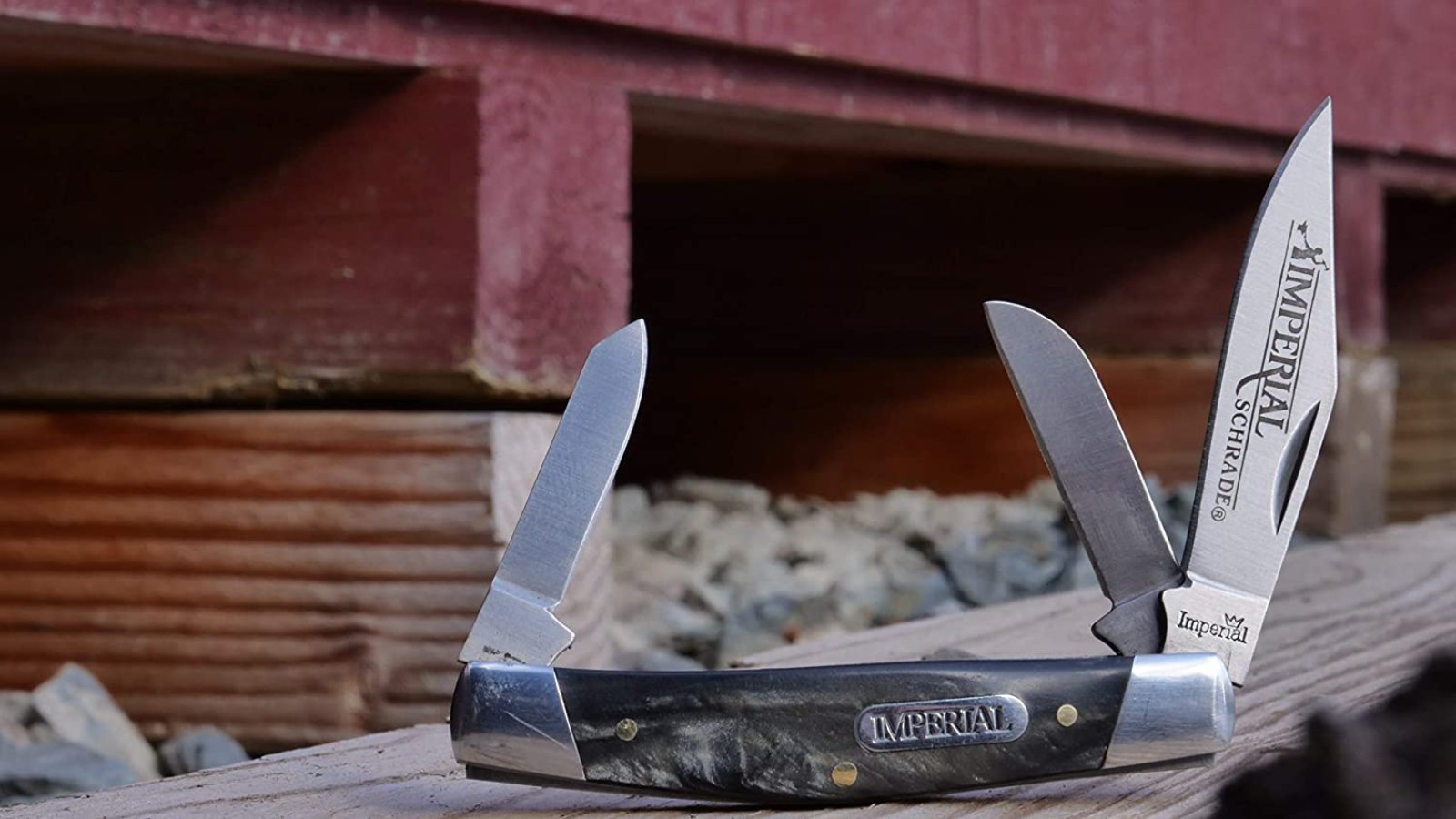 A 3-blade stockman traditional pocket knife sitting on wood beside a red barn.