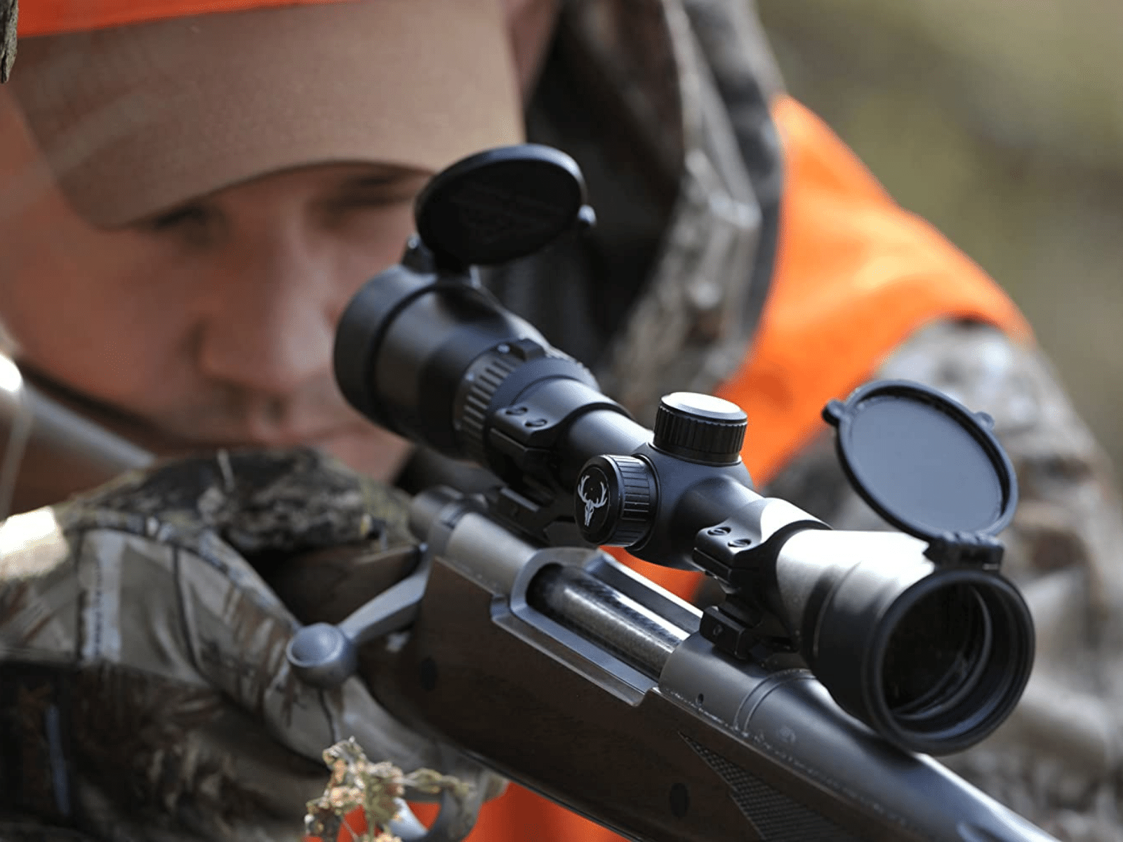 Flip-up scope covers on a rifle being used by a man dressed in camo and hunter orange.