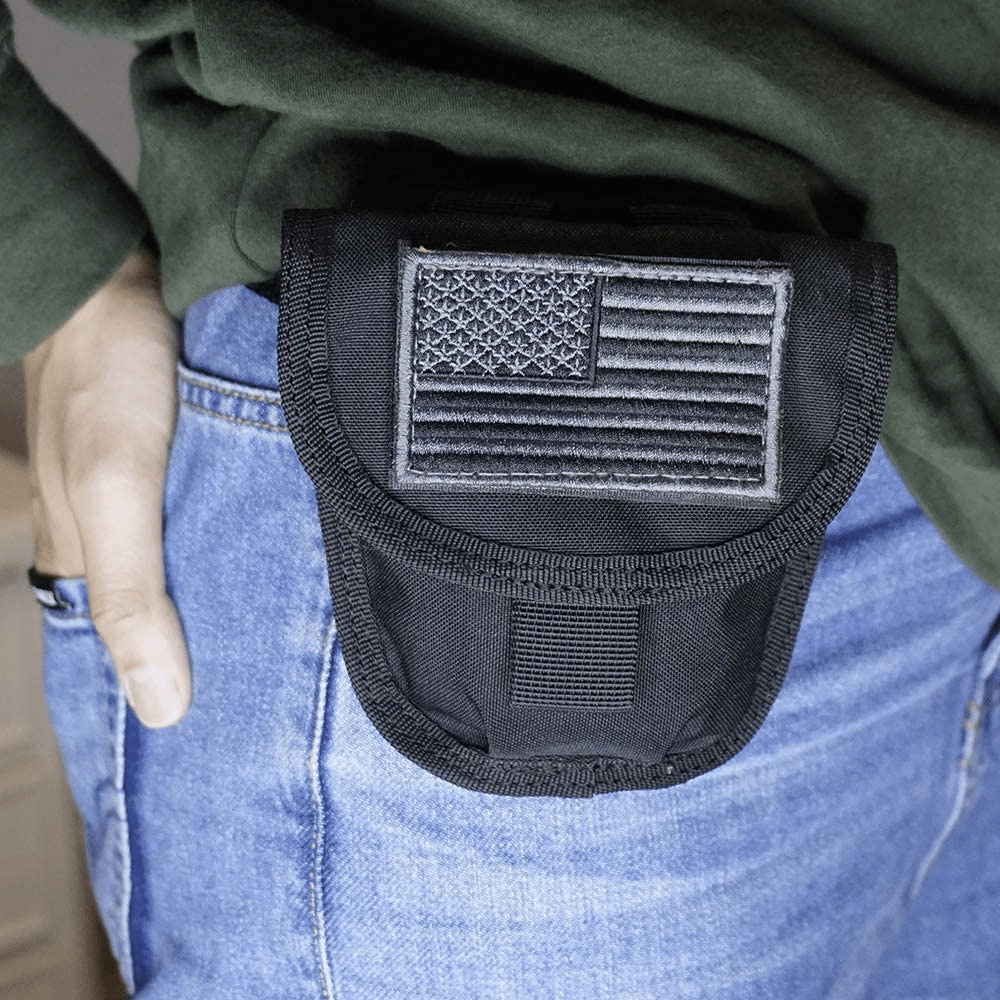 A black handcuff case with a black MOLLE American flag patch on a guy wearing jeans and a green shirt