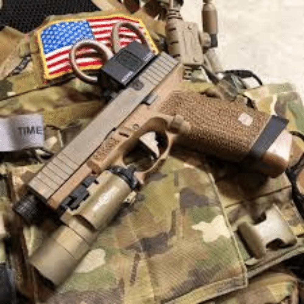 A desert tan Glock 17 with flashlight and optic laying on camo clothing with American flag patch