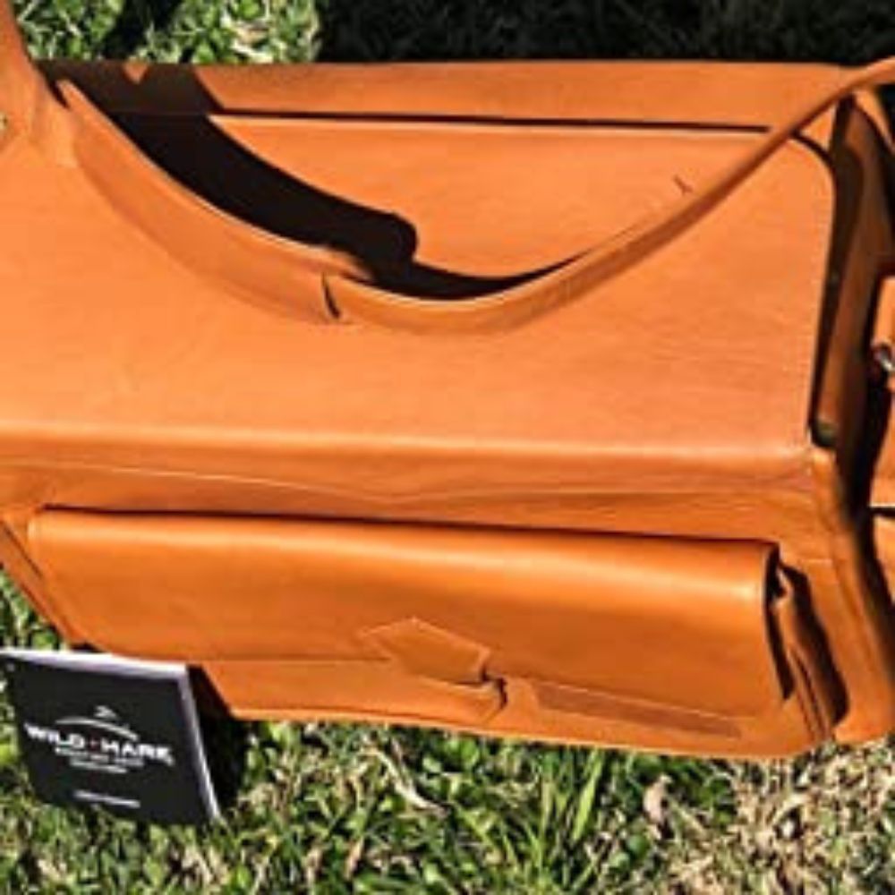 A leather tan colored range bag with shoulder strap sitting in the grass