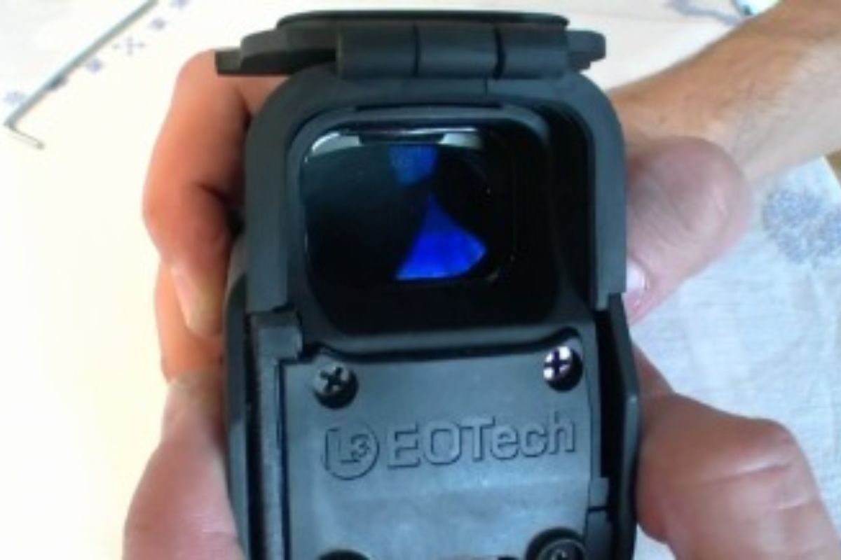 An EOTech pictured in a mans hands with the "pop-up lens cover" open