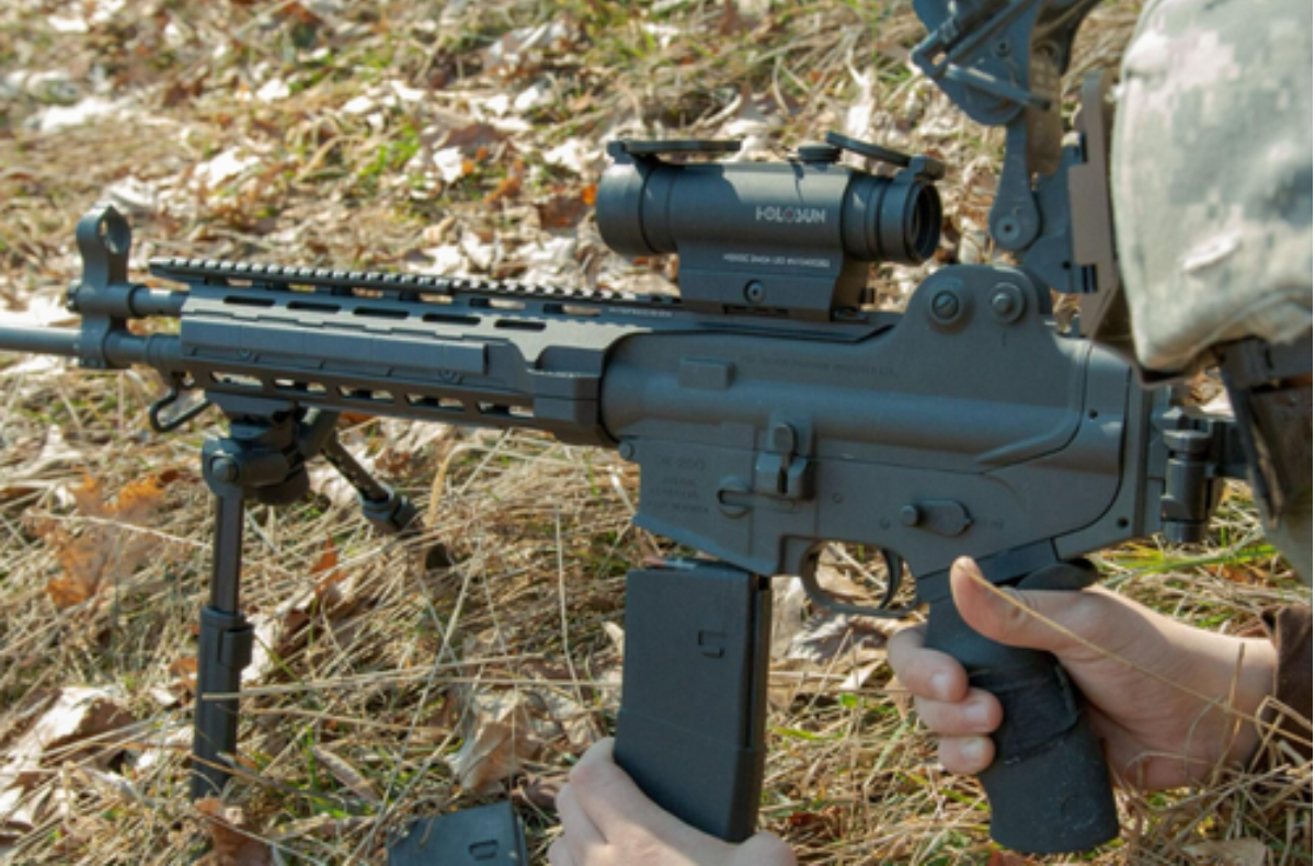 A soldier with his AR15, with Holosun sight, sitting on the bipod changing out Magpul magazines.