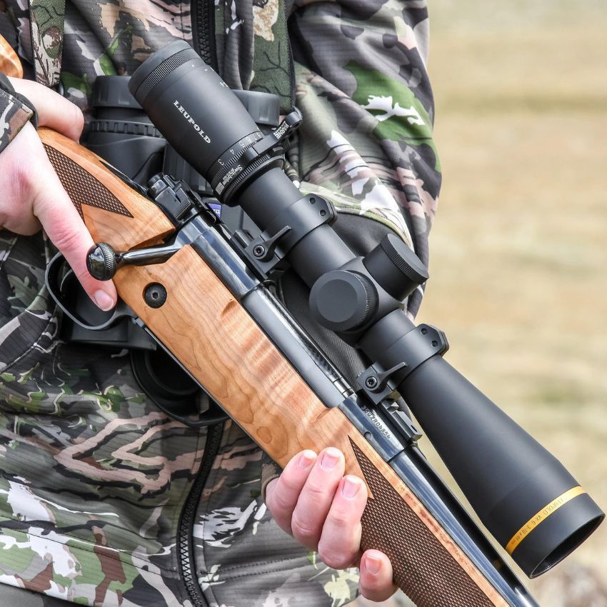 A man in camo holding his Howa 1500 rilfe with a Leupold scope mounted in his Howa 1500 mount