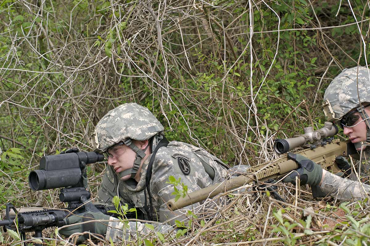 2 soldiers, a sniper and spotter. The spotting scope over the AR15 as he spots for his shooter in thick brush