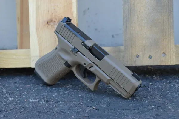 A Glock 19 with FDE slide and frame sitting on the ground next to a wooden door