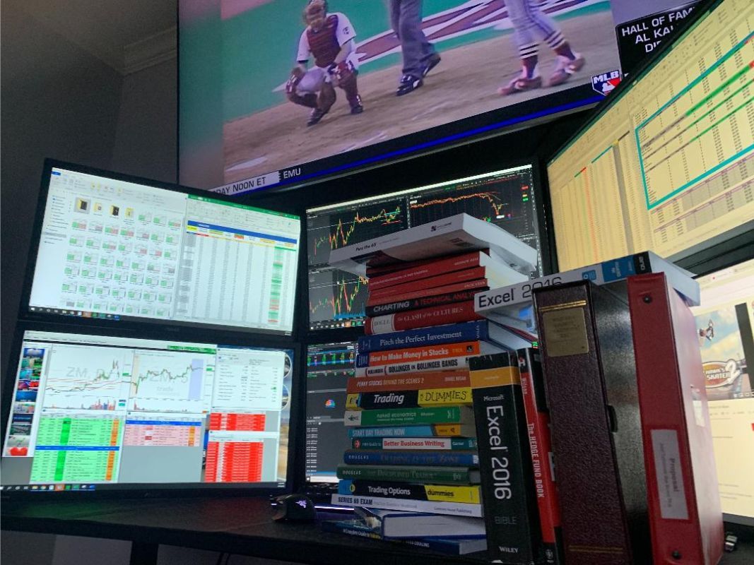 Lots of trading books on a desktop with 4 monitors focusing on day trading