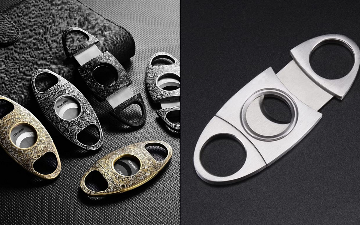 5 cigar cutters laying on a desk with a notebook and a single stainless steel cutter on the counter.