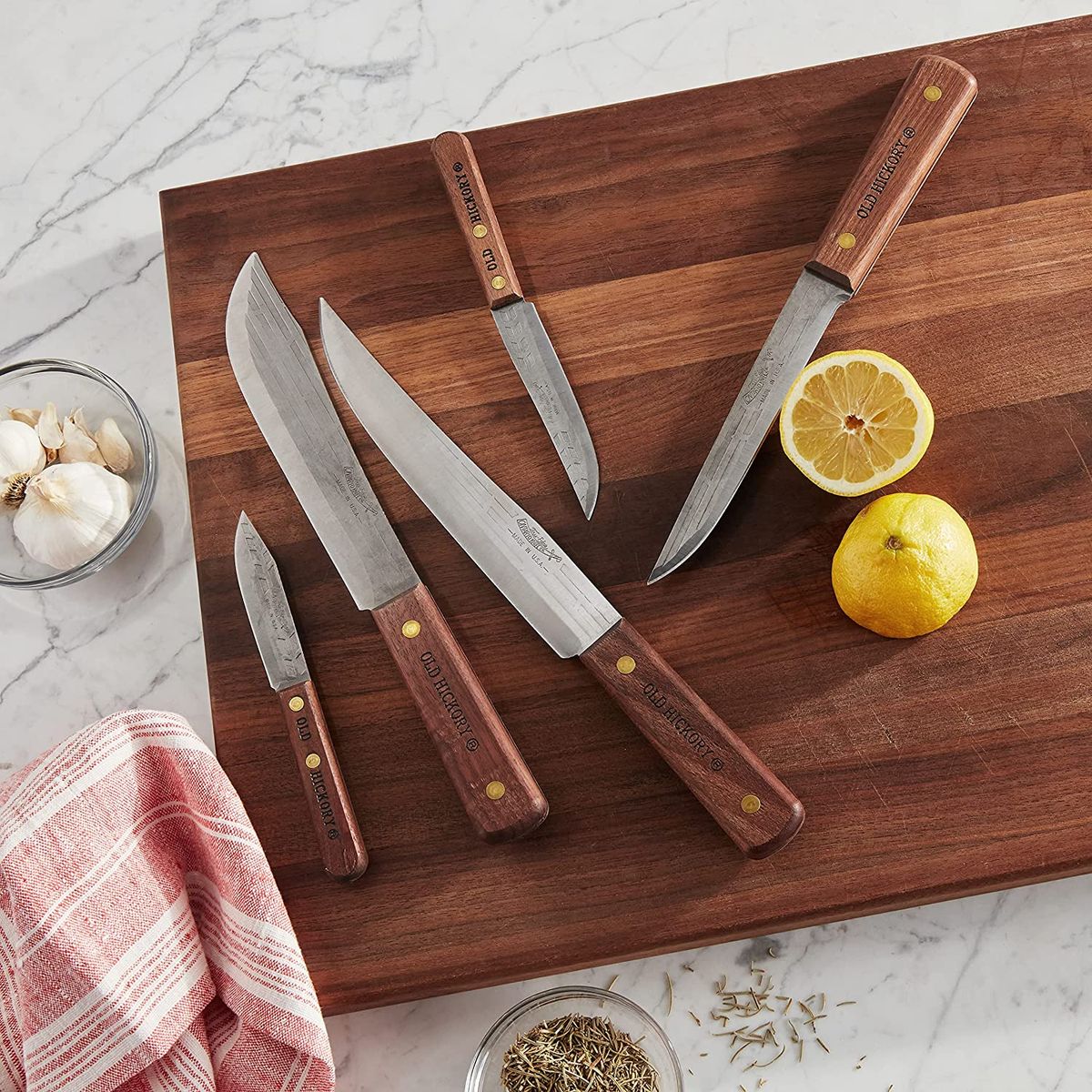 A 5 piece Old Hickory knife set on a cutting board with garlic, lemon, and other spices.