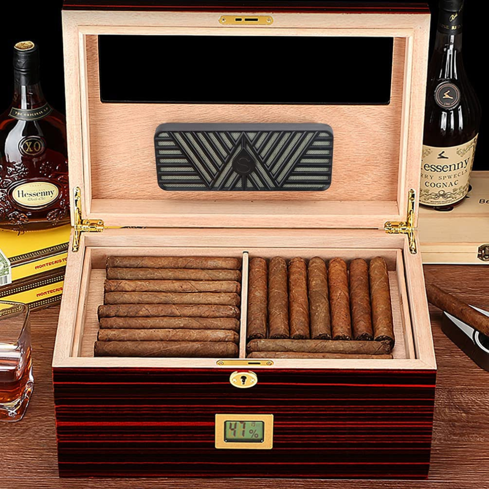 A humidity control humidor with cigars on a table with a whiskey glass and a cigar cutter.