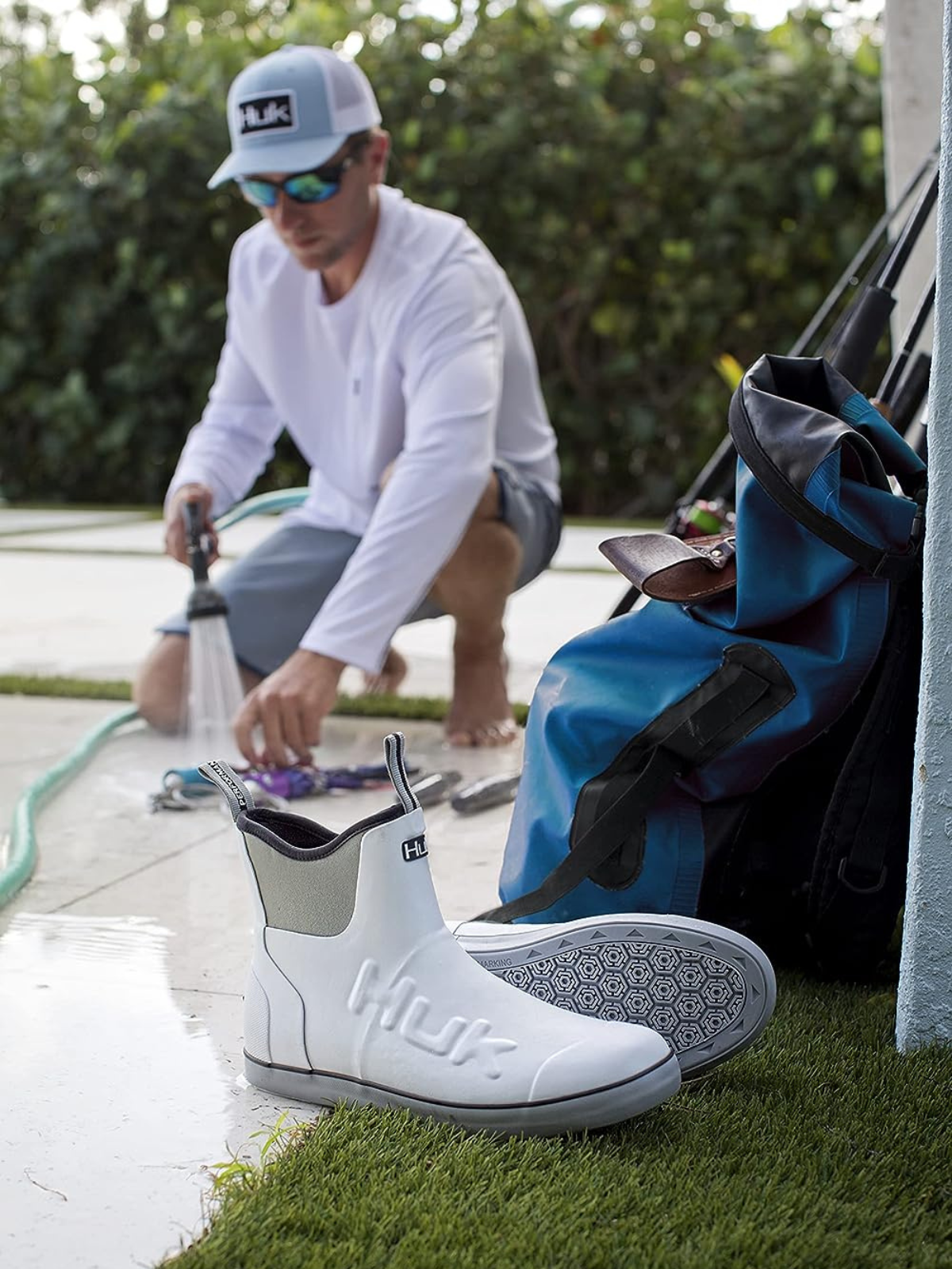 A man beside a pool with a water hose running and a pair of HUK boots sitting on the concrete and grass.