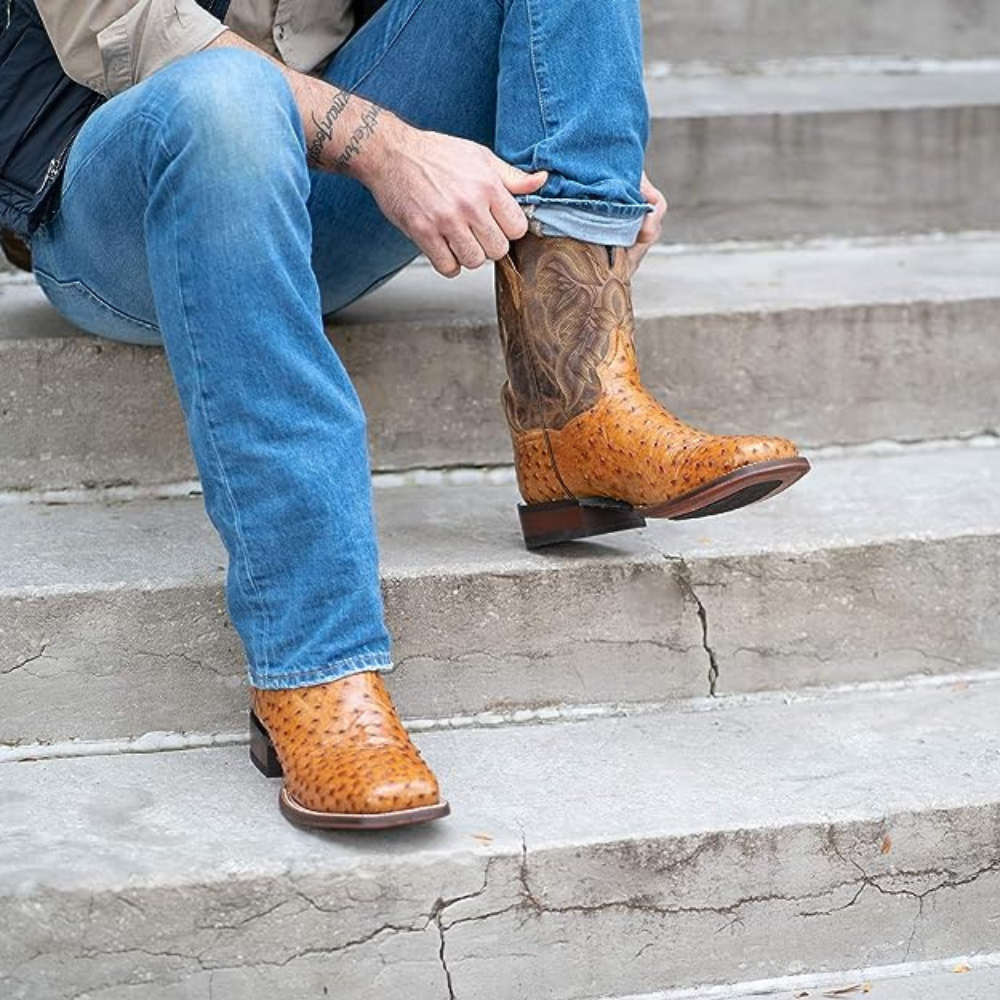 A man sitting on concrete steps putting on his second mens ostrich boot.
