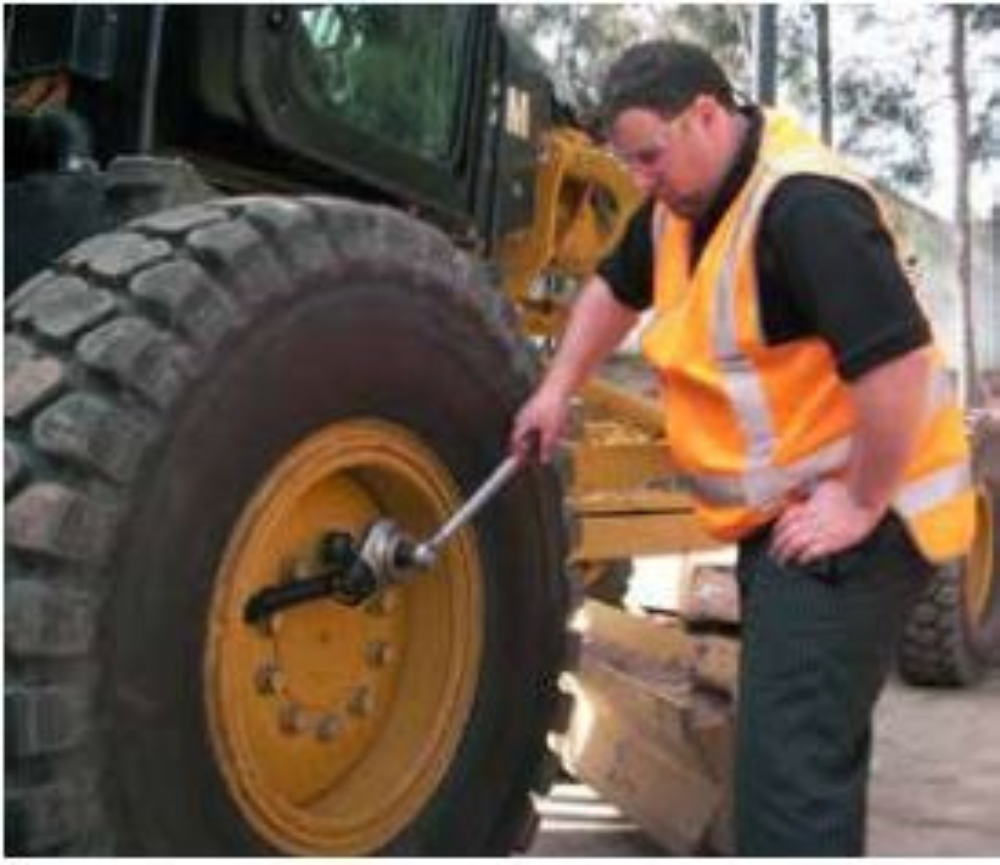 A man tightening a nut on a grader wheel with a torque multiplier