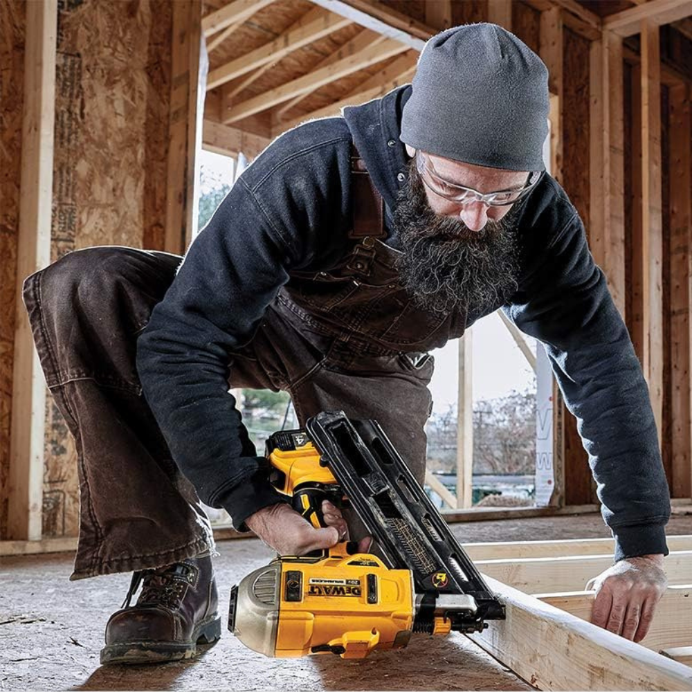 A man using a cordless nailer framing a wall in a new home build.