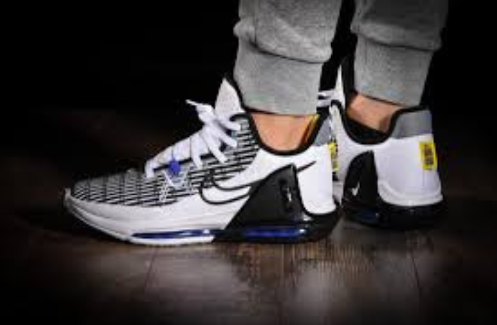 Closeup of a man wearing white/black/blue LeBron Witness 6 shoes on real hardwood floor.