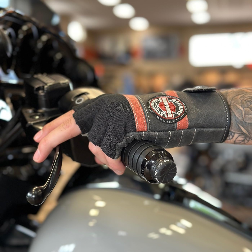 A mans left hand on the handlebars of a Harley-Davidson with a pair of their riding gloves on.