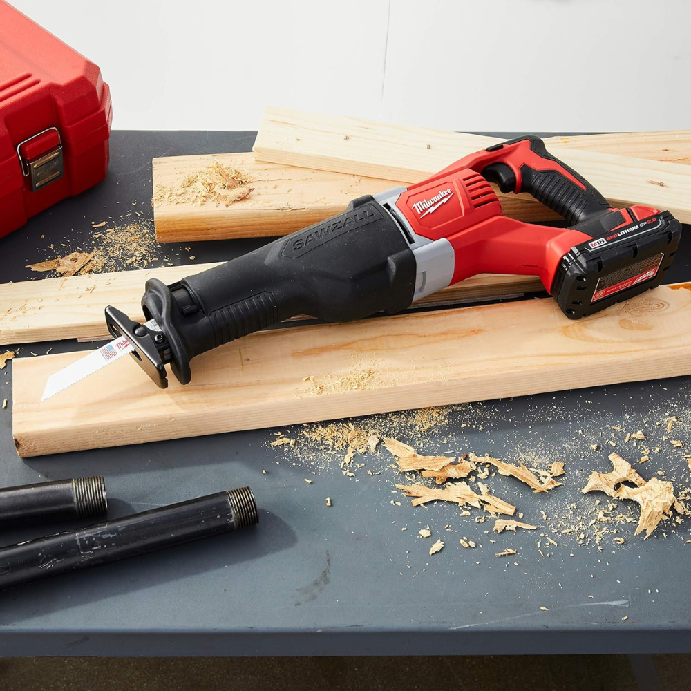 A cordless sawzall laying on some boards on a gray table with pieces of pipe and sawdust.