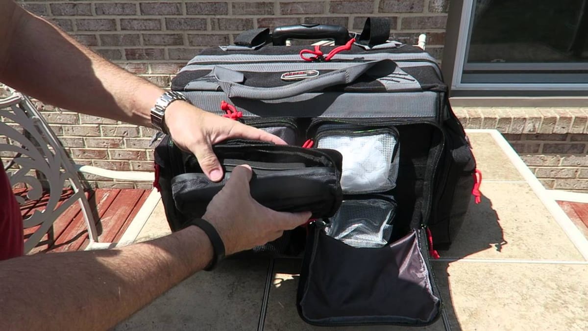 A man opening the side pockets of his rolling range bag next to a brick house.