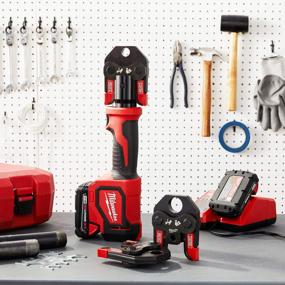 Cordless PEX crimping tools sitting on a workbench with a charger/battery, case and 2 pieces of pipe.