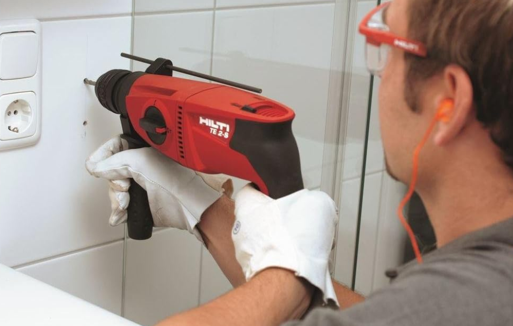 A man drilling into tile on the wall with a hammer drill.