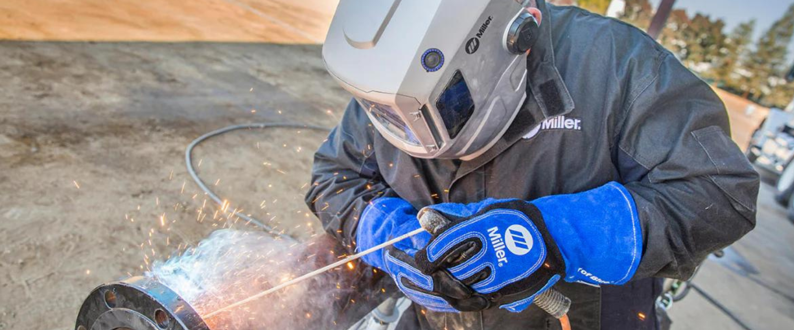A man welding pipe with a stick welder and wearing Miller Welding gloves, suit, and helmet.