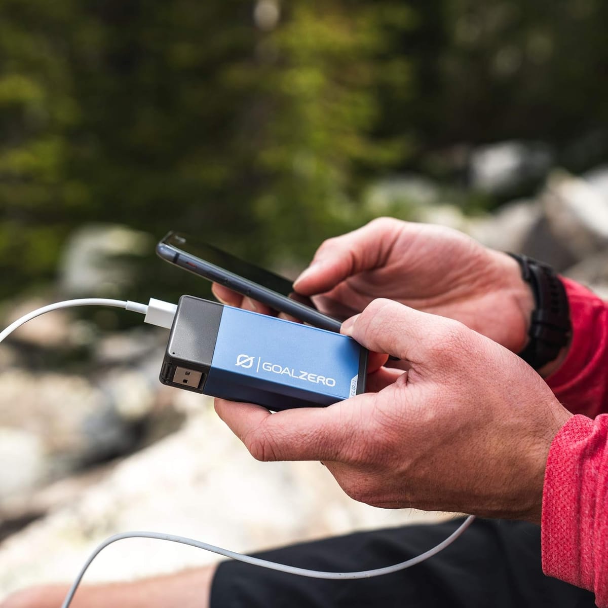 A man holding a blue power bank hooked to his cell phone.