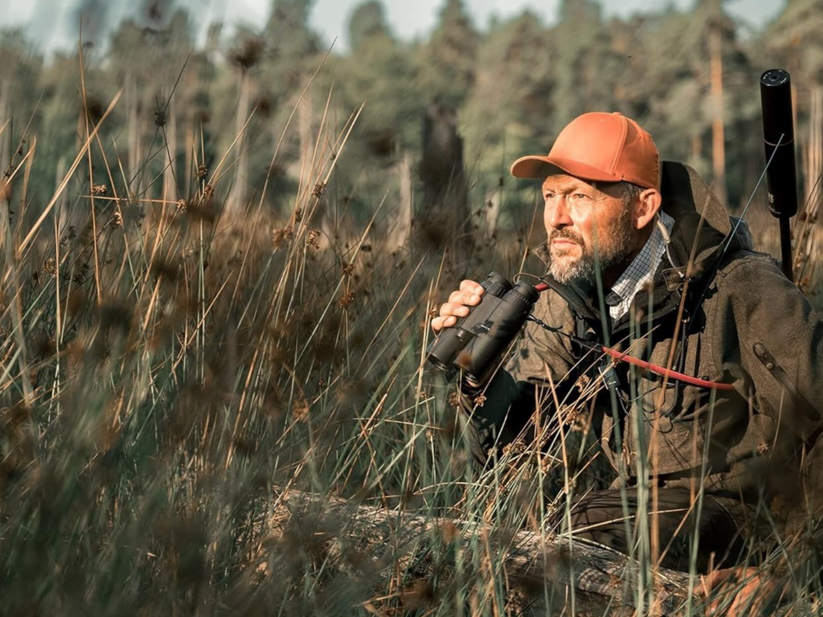 A man in camo sitting in tall grass with his range finding binos looking for a shot at a trophy!