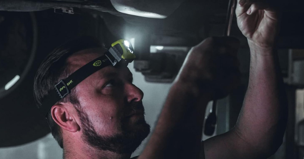 A man working underneath a car wearing a headlamp