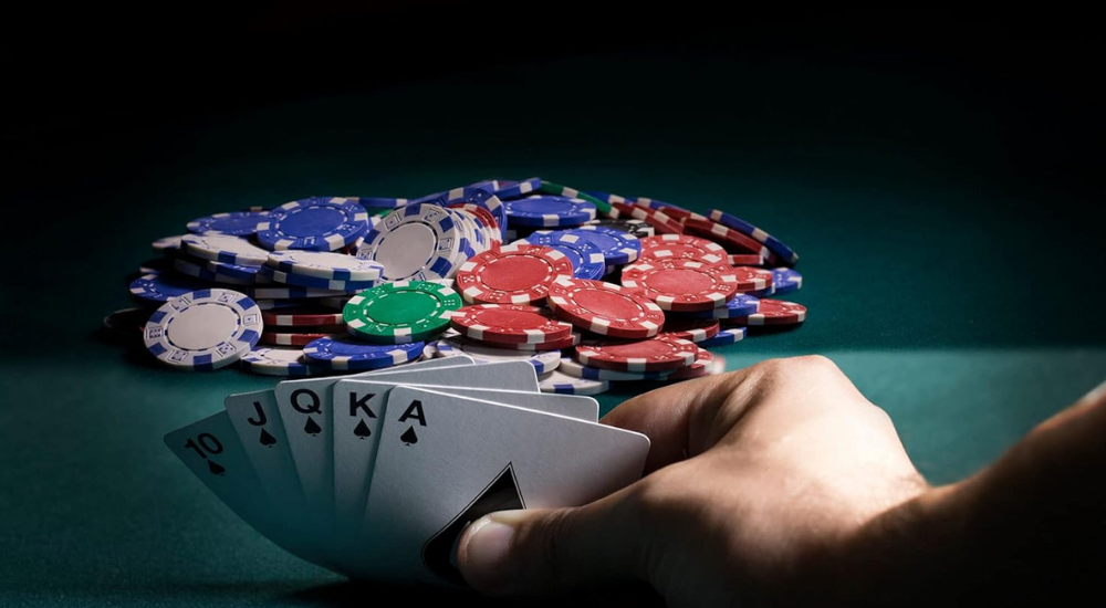 A man holding a straight flush looking at a pile of poker chips.