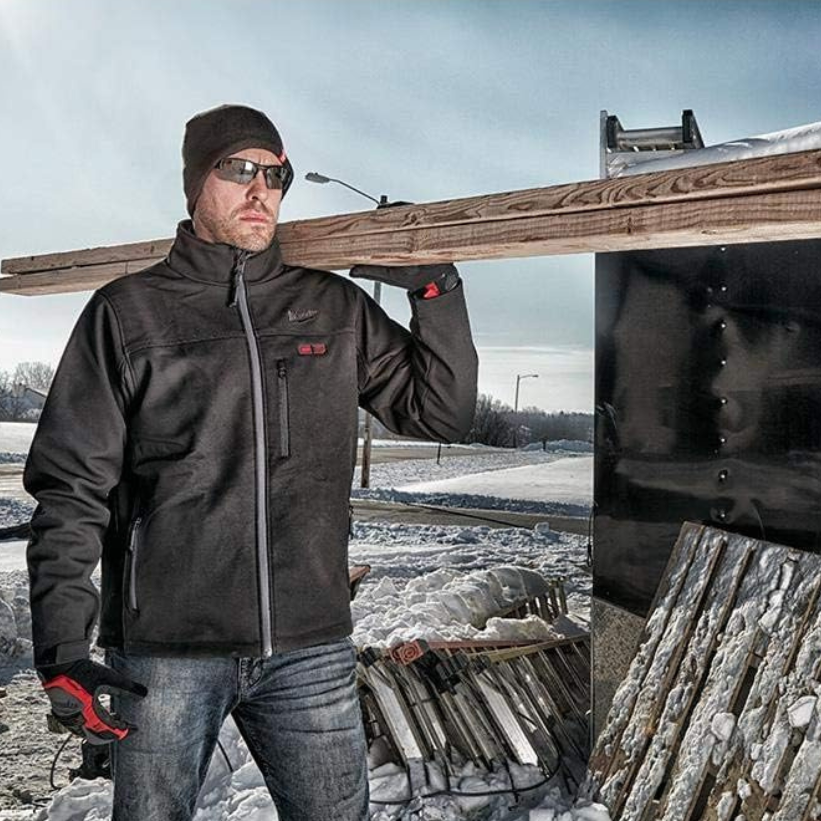 A man carrying wood in the snow while wearing a heated jacket using the M12 Milwaukee battery